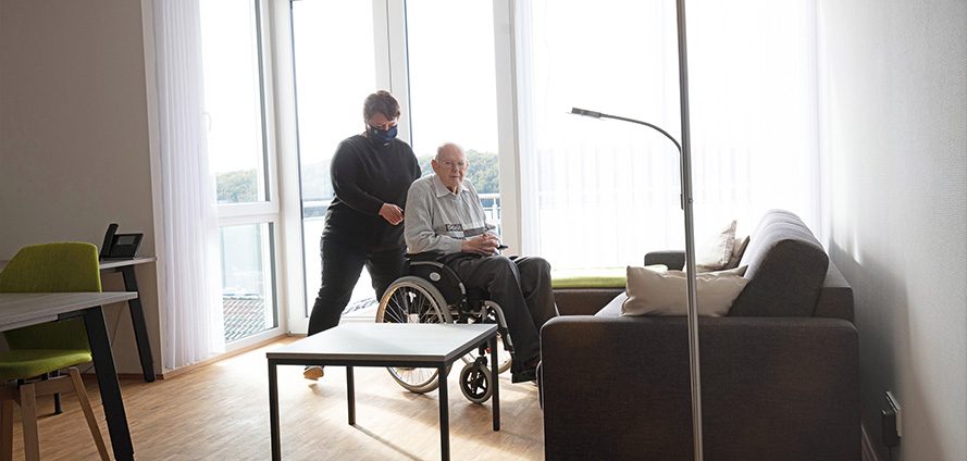 Rollstuhlfahrer mit Begleitung im Wohnraum einer Wohnung des Tönsberghauses